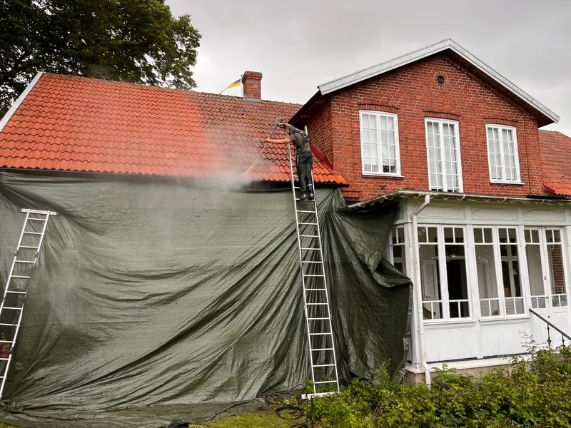 Mossro utför taktvätt på rött tegeltak i Skåne med presenning som skyddar fasaden